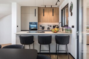 Una cocina moderna con una isla central, taburetes de bar, horno empotrado y cafetera.