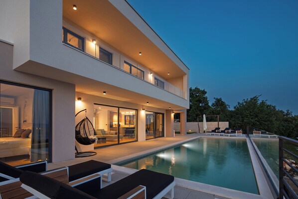 Une maison moderne à deux étages, dotée d’une piscine, d’un espace extérieur aménagé et d’un salon entièrement vitré.