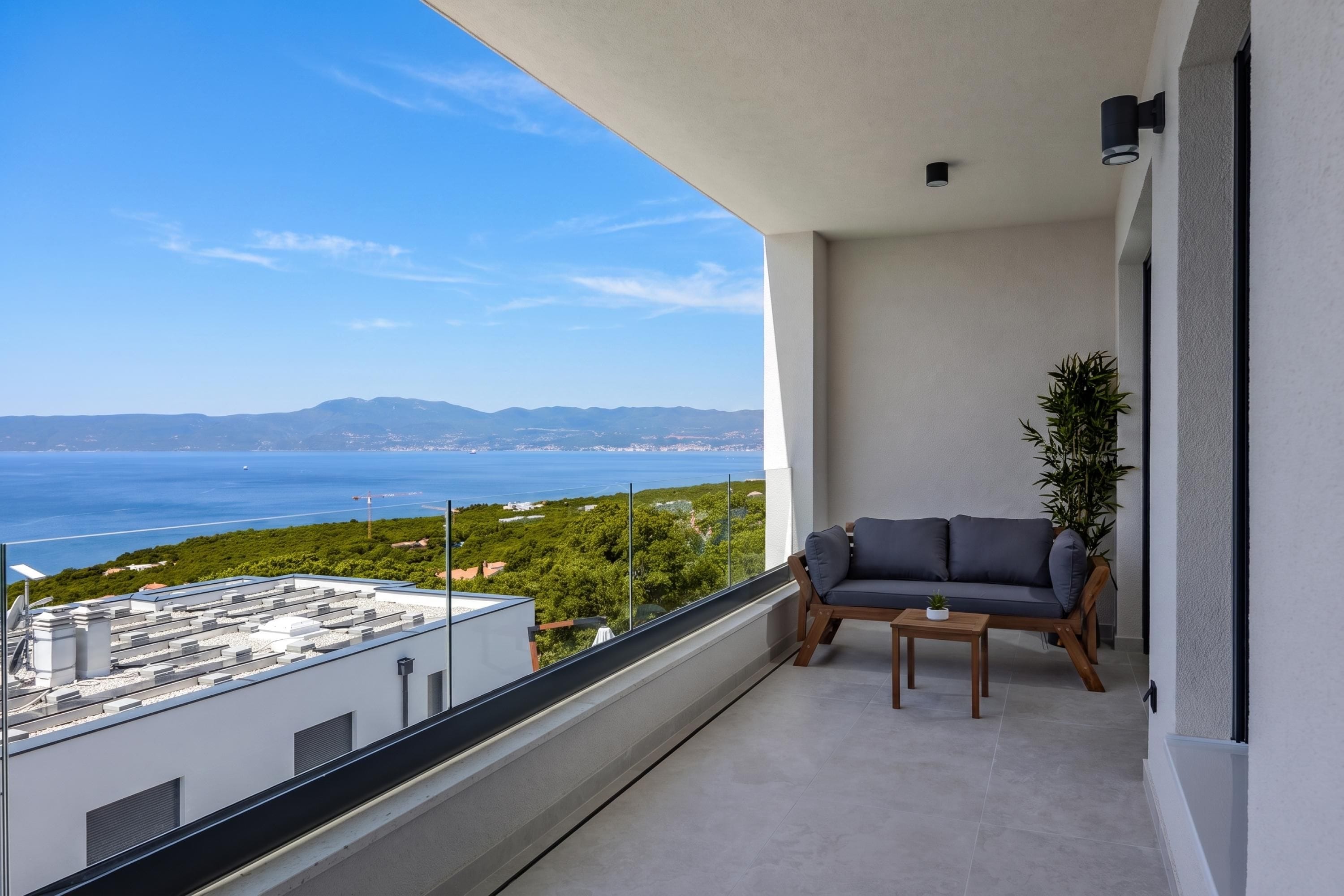 A balcony with a view of the sea, a sofa, and a potted plant.