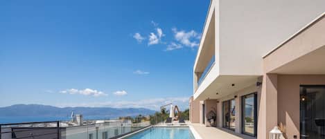 Un edificio moderno con piscina en la azotea, vistas despejadas al mar y montañas al fondo.