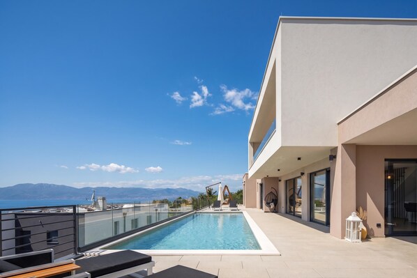 A modern building with a rooftop pool, a clear view of the sea, and mountains in the background.