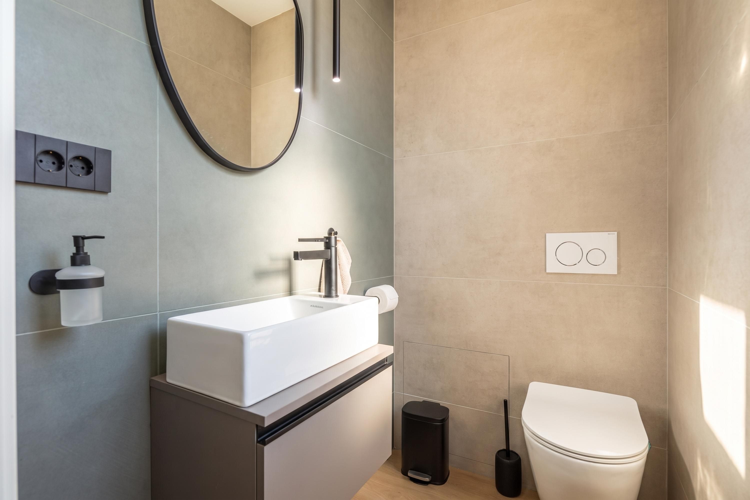 Ein modernes Badezimmer mit einem weißen Waschbecken, einem Spiegel, einer Toilette und einem Mülleimer.