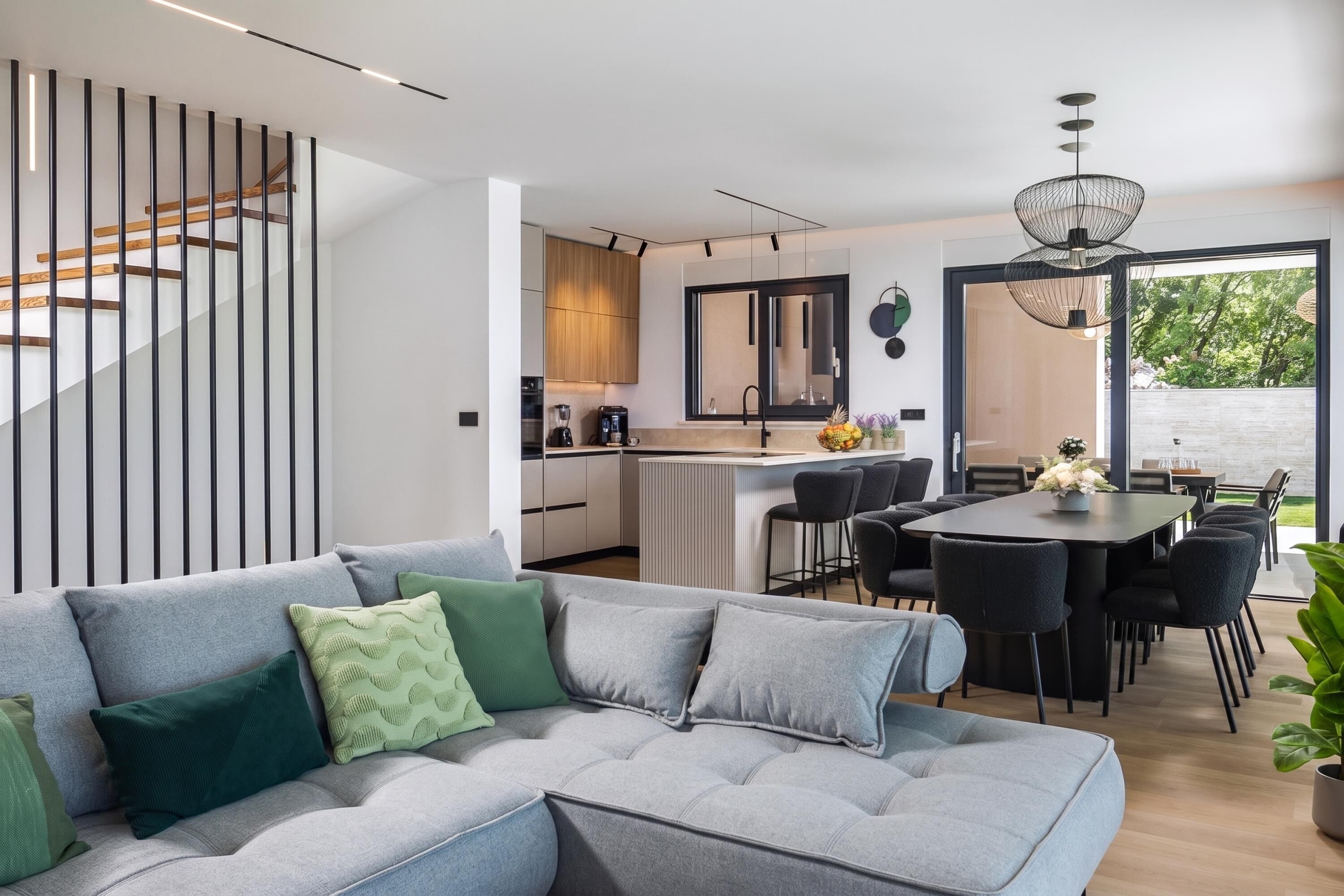 A modern kitchen with a dining area, a sofa with cushions, and a staircase.