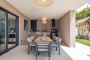 A modern outdoor dining area with a table and chairs, a grill, and a view of the backyard.