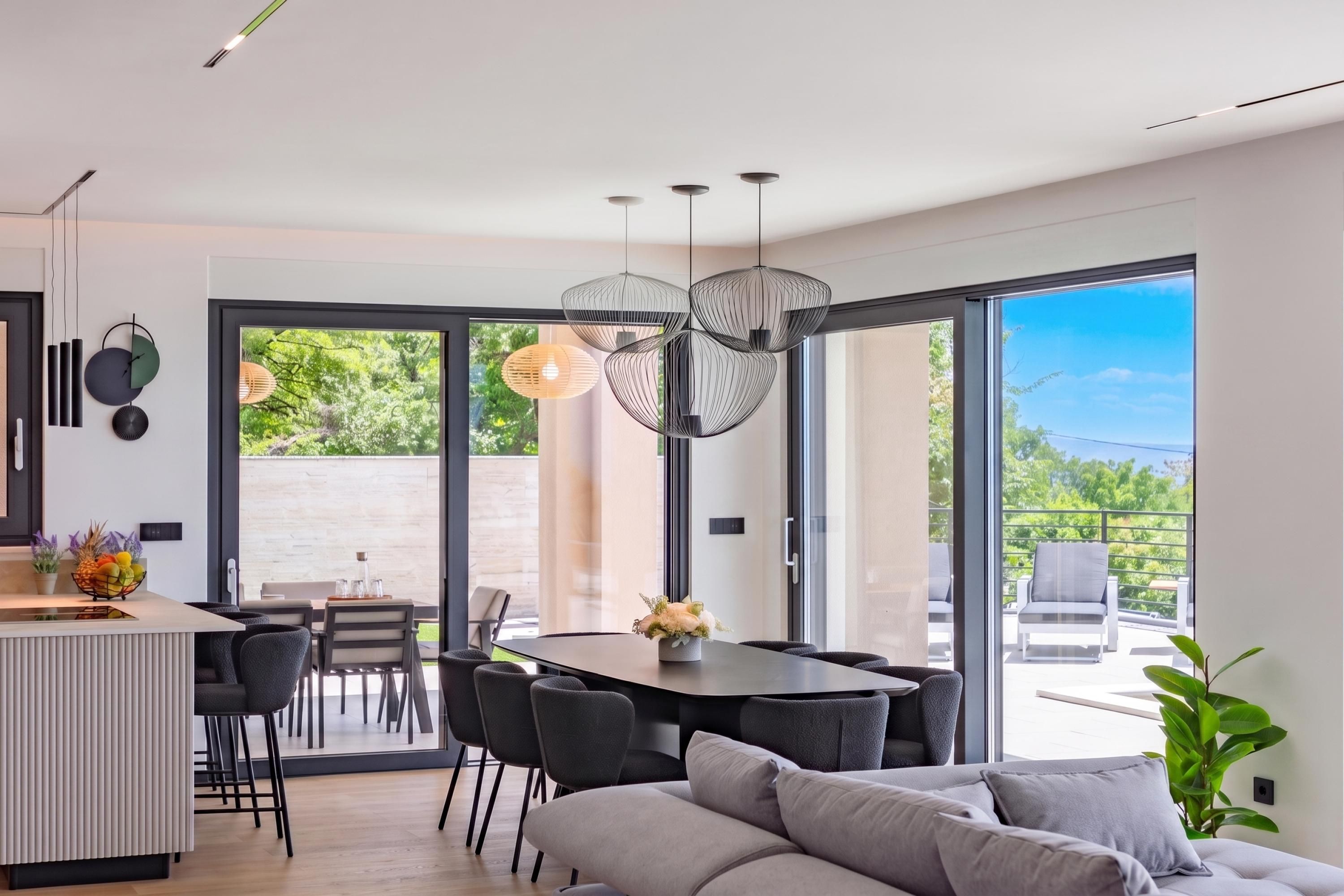 Un interior moderno con zona de comedor, sofá y un amplio ventanal con vistas a zonas verdes.