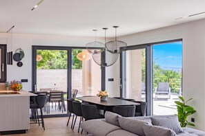 A modern interior with a dining area, a sofa, and a large window offering a view of greenery.