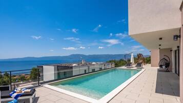 A rooftop infinity pool with a clear view of the sea and mountains.