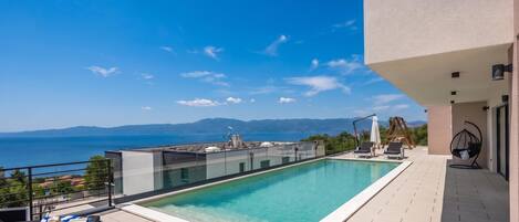 Piscina infinita no terraço com vista desimpedida para o mar e montanhas.