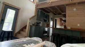 Una habitación estilo loft con zona de cocina, vigas de madera en el techo y una ventana.