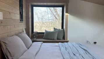 Ein Schlafzimmer mit Holzbalkendecke, einem großen Fenster, einem Bett mit Kissen und einem Nachttisch.
