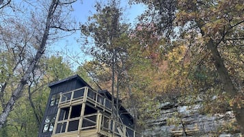 Une cabane en bois dotée d’un balcon, entourée d’arbres et d’une falaise rocheuse.