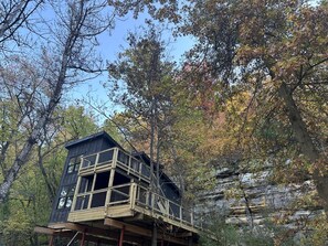 A wooden cabin with a balcony, surrounded by trees and a rocky cliff. - Luxury Treehouse Retreat with Stunning Decks & Creek Access Near Starved Rock State Park, Ottawa, IL (Ottawa)