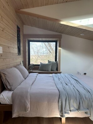 A bedroom with a wooden ceiling, a large window, a bed with pillows, and a bedside table. - Luxury Treehouse Retreat with Stunning Decks & Creek Access Near Starved Rock State Park, Ottawa, IL (Ottawa)
