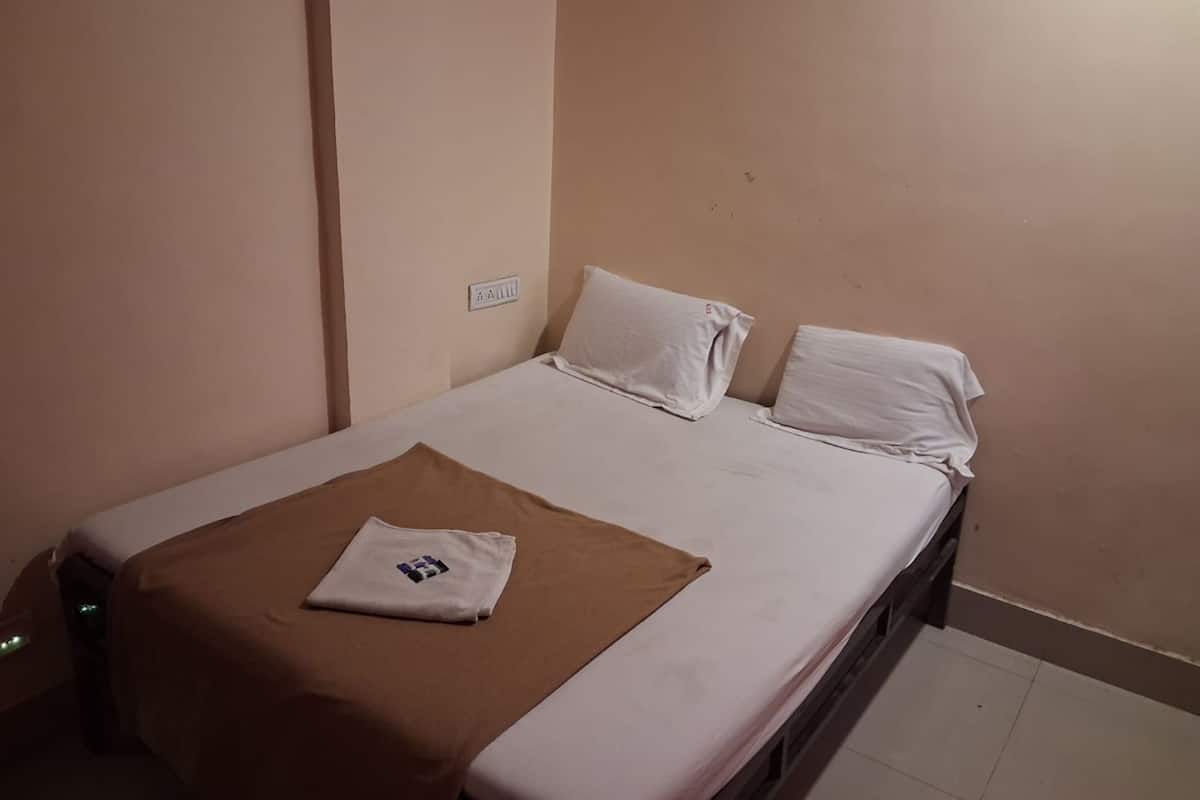 Una cama individual con sábanas blancas, una colcha marrón y dos almohadas.