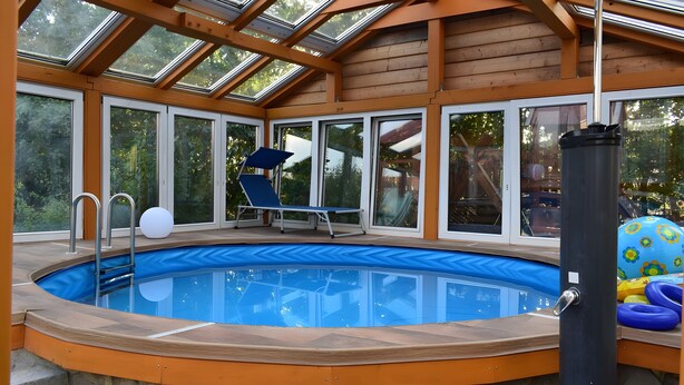 En pool med en glasvägg runt om, en solstol och ett område vid poolkanten.