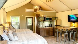 A tented accommodation with a bed, kitchenette, dining area, and a TV.