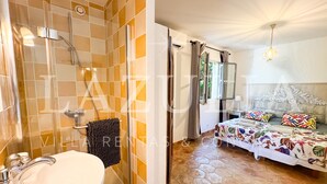 A bathroom with a glass shower enclosure, a sink, and a toilet. The bedroom features a bed with a floral bedspread, a nightstand, and a window with curtains. - Villa Boucheron - 4 independent apartments - Sea view (Roquebrune-sur-Argens)