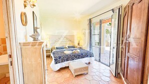 A bedroom with a large bed, a wooden bench, a nightstand, and a sliding glass door leading to an outdoor area. - Villa Boucheron - 4 independent apartments - Sea view (Roquebrune-sur-Argens)