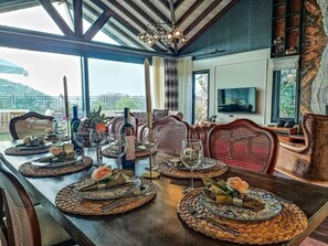 Ein Essbereich mit einem langen Tisch, der für eine Mahlzeit gedeckt ist, einem Fernseher und schöner Aussicht.