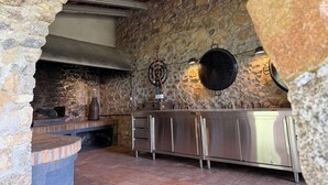 A stone-walled kitchen with a stone archway, a hanging pot rack, and a built-in oven. - At the foot of the Pyrenees (Maçanet de Cabrenys)