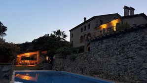 A swimming pool with a stone wall and a building with arched windows. - At the foot of the Pyrenees (Maçanet de Cabrenys)