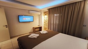 Ein Hotelzimmer mit Bett, Wandfernseher, Klimaanlage, kleinem Tisch und Vorhang.