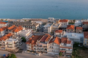 An aerial view of a coastal residential area with buildings, a beach, and a road. - Elisa Luxury Suite in Nea Flogita (Flogita)