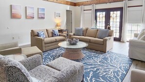 A spacious living room with two sofas, a coffee table, patterned ottomans, and a large window with curtains. - 600 Steps, Great Family Beach House, Pet friendly & Close to Beach (Pawleys Island)