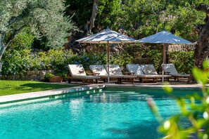 A pool with clear water, surrounded by lounge chairs and umbrellas, set against a backdrop of trees and a stone wall. - Spacious 9-bedroom private villa with AC in lovely Sóller (Sóller)