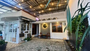 A spacious indoor area with a tiled floor, a seating area with chairs, a large window, and a wall-mounted speaker system.