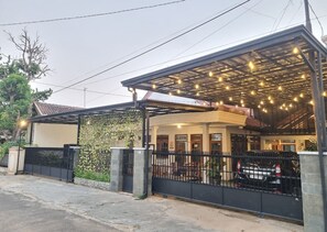A covered outdoor area with a metal roof, a black fence, and a car parked inside. - DJS Homestay Syariah (Bandar Lampung)
