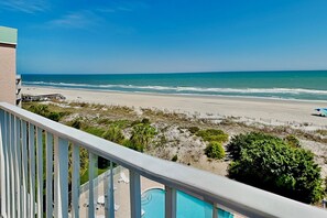 A balcony with a view of a beach and ocean, a pool, and a wooden deck. - Hamilton 502- Direct Ocean View from Top Floor (Pawleys Island)