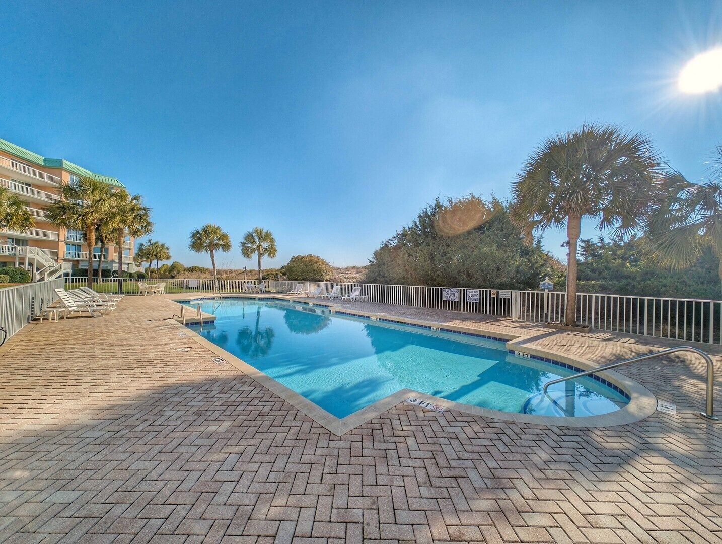 A swimming pool with a brick deck, lounge chairs, and palm trees.