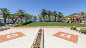 Ein gepflasterter Weg mit Palmen und einer Rasenfläche, der zum Strand führt.