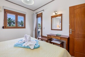 A hotel room with a bed, a desk, a chair, a wooden door, a mirror, and a window with curtains. - Family Beachfront Apartment with Sea View in Agia Galini, Crete (Agia Galini)