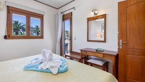 Habitación de hotel con cama, escritorio, silla, puerta de madera, espejo y ventana con cortinas.