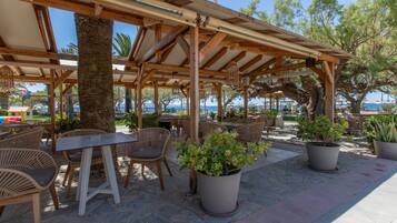 Une terrasse extérieure avec des tables et des chaises en bois, des plantes en pot et une vue sur la mer.