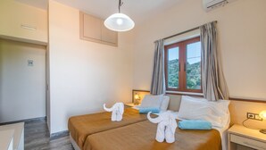 A hotel room with two beds, a window with curtains, a bedside table with a lamp, and a view of the outdoors.