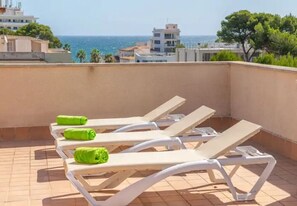 A rooftop terrace with white sun loungers and green towels, overlooking a coastal cityscape. - Apartment Son Baulo Sindria (Ca´n Picafort)
