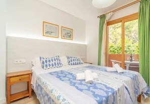 A bedroom with a bed, a nightstand, a window with curtains, and two framed pictures on the wall. - Apartment Son Baulo Sindria (Ca´n Picafort)