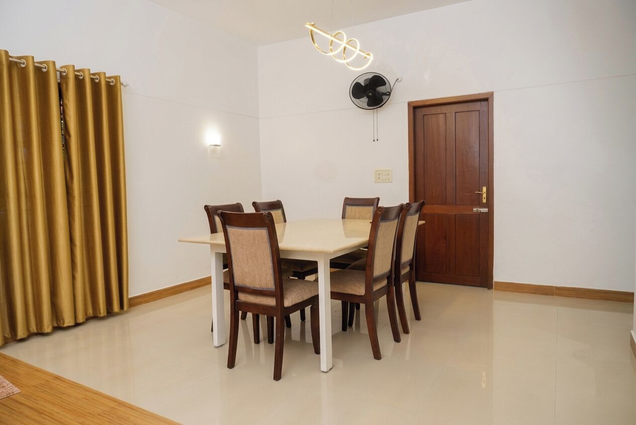 Un comedor con una mesa, sillas, un ventilador de techo, una puerta y cortinas.