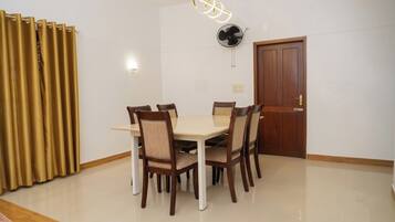 Un comedor con una mesa, sillas, un ventilador de techo, una puerta y cortinas.