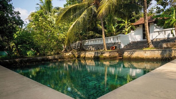 A clear pool surrounded by lush greenery and a white building with a red roof. - Vayal Varam Private Villa Peaceful Nature Stay Kollam (Kollam)