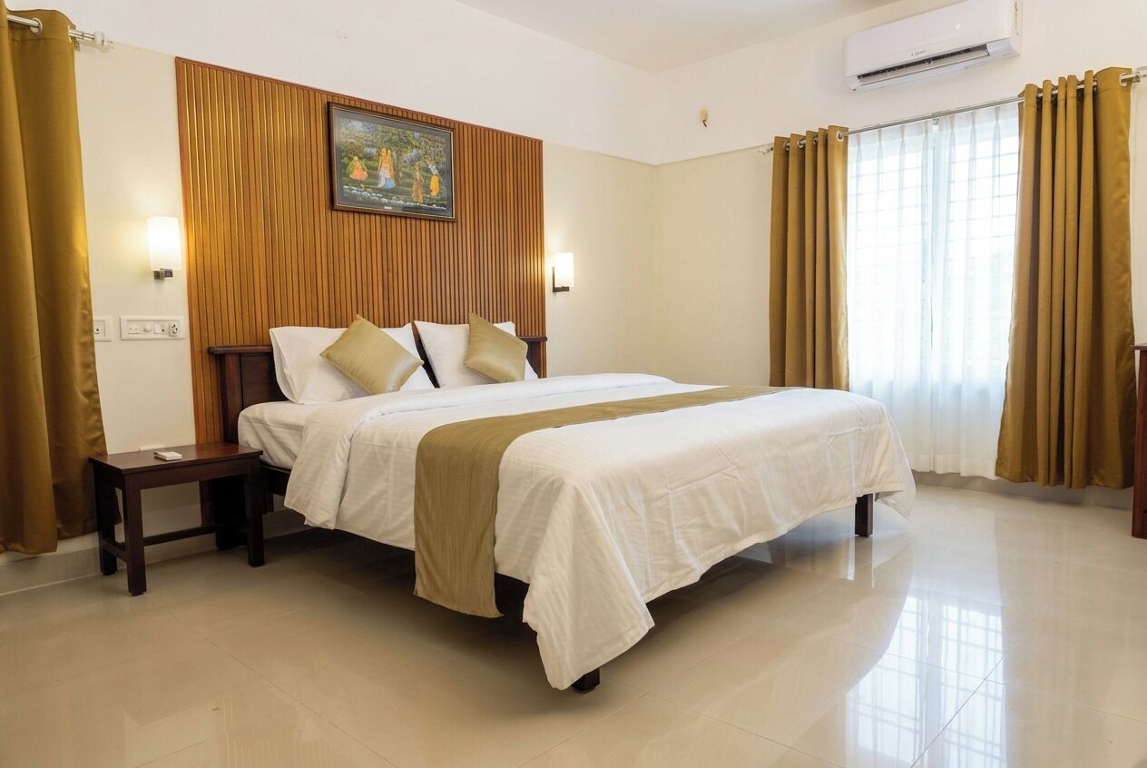 A hotel room with a large bed, wooden paneling on the wall, a painting, and an air conditioning unit.