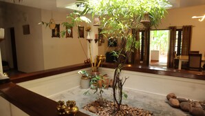 A room with a large indoor plant, a wooden reception desk, and a stone-tiled floor. - Vayal Varam Private Villa Peaceful Nature Stay Kollam (Kollam)