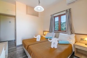 Habitación de hotel con dos camas, una ventana con cortinas, una mesita de noche con lámpara y vistas al exterior.