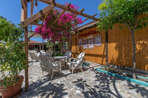 Eine Terrasse mit Korbstühlen, einer Holzpergola und einem Schild.
