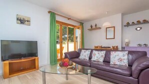 A living room with a TV, glass coffee table, purple sofa, and a sliding glass door. - Apartment Son Baulo Pera (Ca´n Picafort)