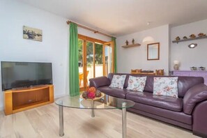 Ein Wohnzimmer mit Fernseher, Glastisch, violettem Sofa und einer Schiebetür aus Glas.