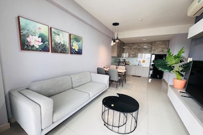 Una sala moderna con un sofá gris, una mesa de centro negra y un comedor con sillas. Hay tres cuadros florales enmarcados en la pared.